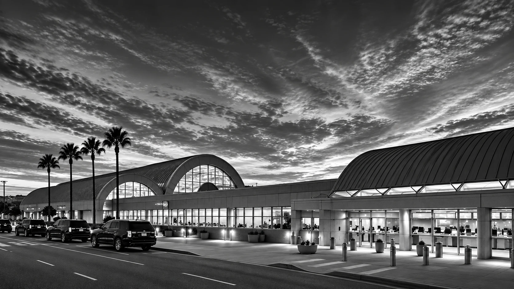 John Wayne Airport terminal exterior with palm trees and luxury SUVs in black and white